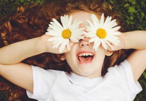 Child with daisy eyes, on green grass in a summer park.